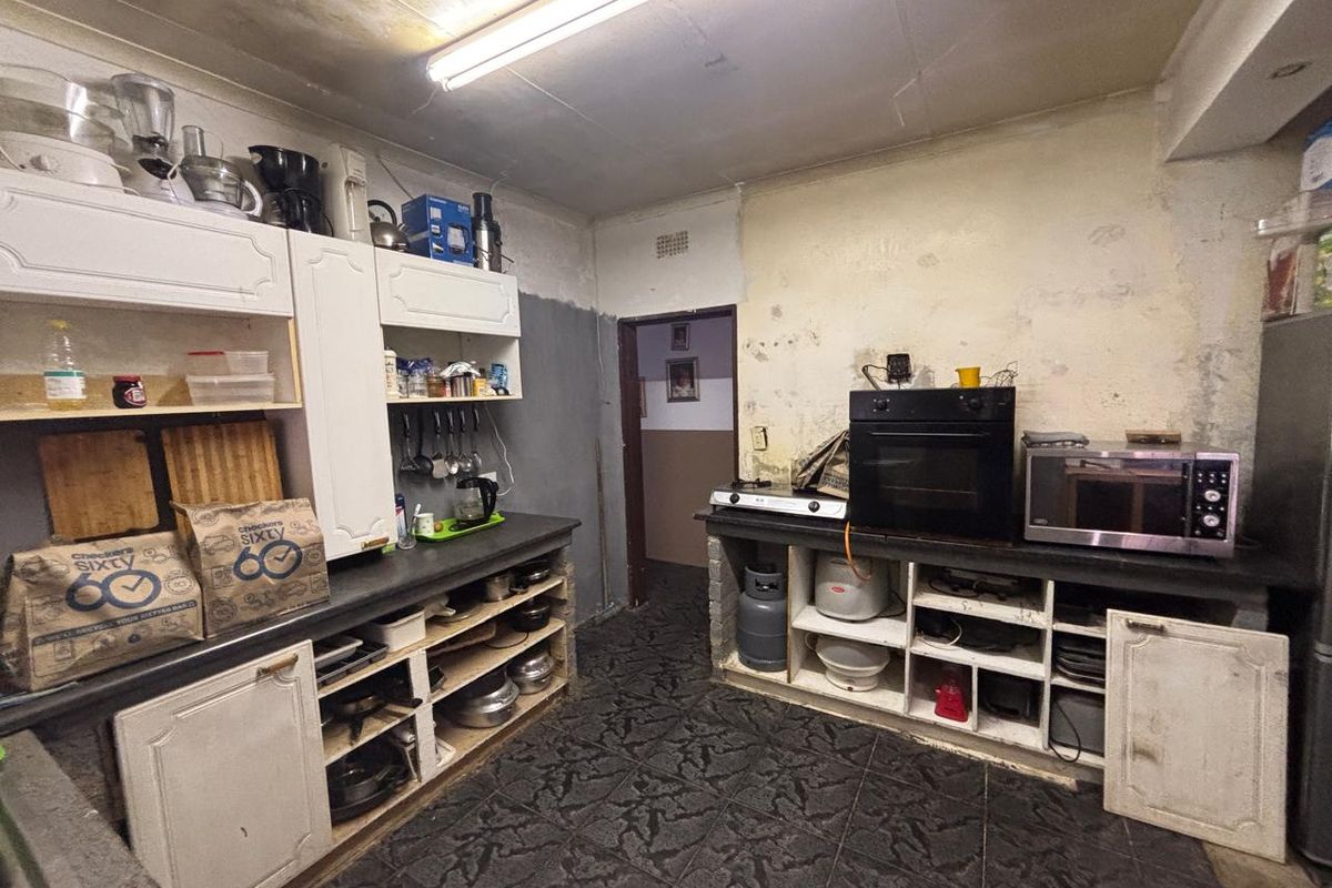 A dated kitchen featuring built-in cabinetry, stone countertops, and a built-in oven, requiring significant cosmetic renovation and wall repairs.