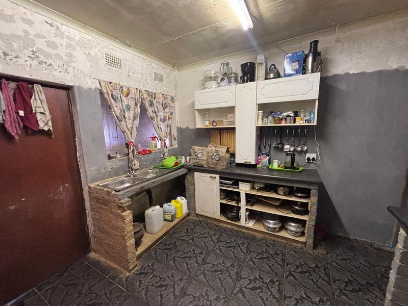 A functional kitchen area featuring brick-based cabinetry, a double basin sink, and tiled flooring, currently requiring significant cosmetic renovation and wall finishing.