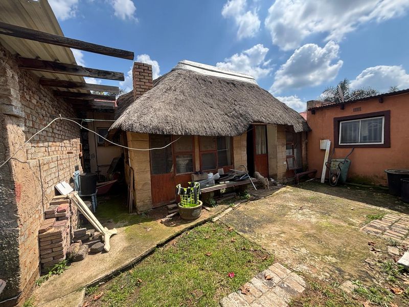 Rear exterior view of a property featuring a traditional thatch roof, exposed brickwork, and a paved courtyard area requiring maintenance.