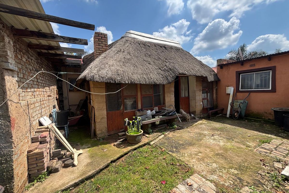 Rear exterior view of a property featuring a traditional thatch roof, exposed brickwork, and a paved courtyard area requiring maintenance.