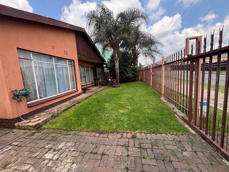 Front exterior view of the property featuring a paved driveway, lawn area, and secure metal perimeter fencing.