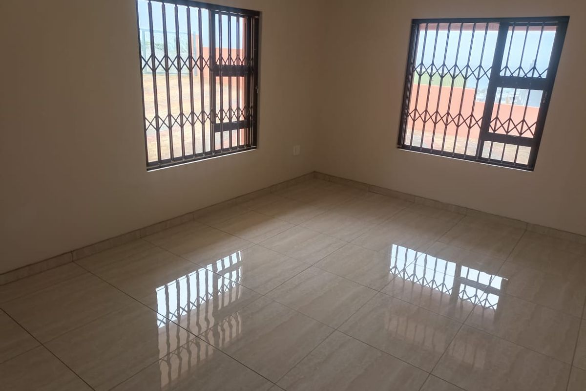 A bright, empty bedroom featuring neutral tiled flooring and windows fitted with security bars.