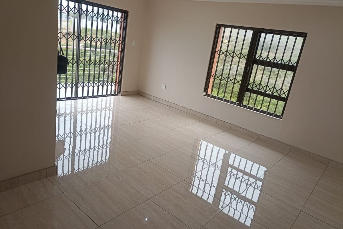 A bright, empty living area featuring polished porcelain floor tiles, security gates, and burglar bars, offering a clean and neutral space ready for furnishing.