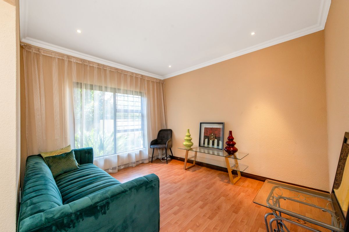 A living room featuring laminate flooring, recessed ceiling lighting, and a large window with sheer curtains.