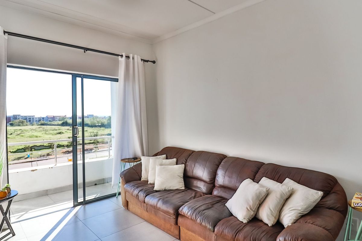 A bright living room featuring tiled flooring and a large sliding glass door that provides direct access to an outdoor balcony area.