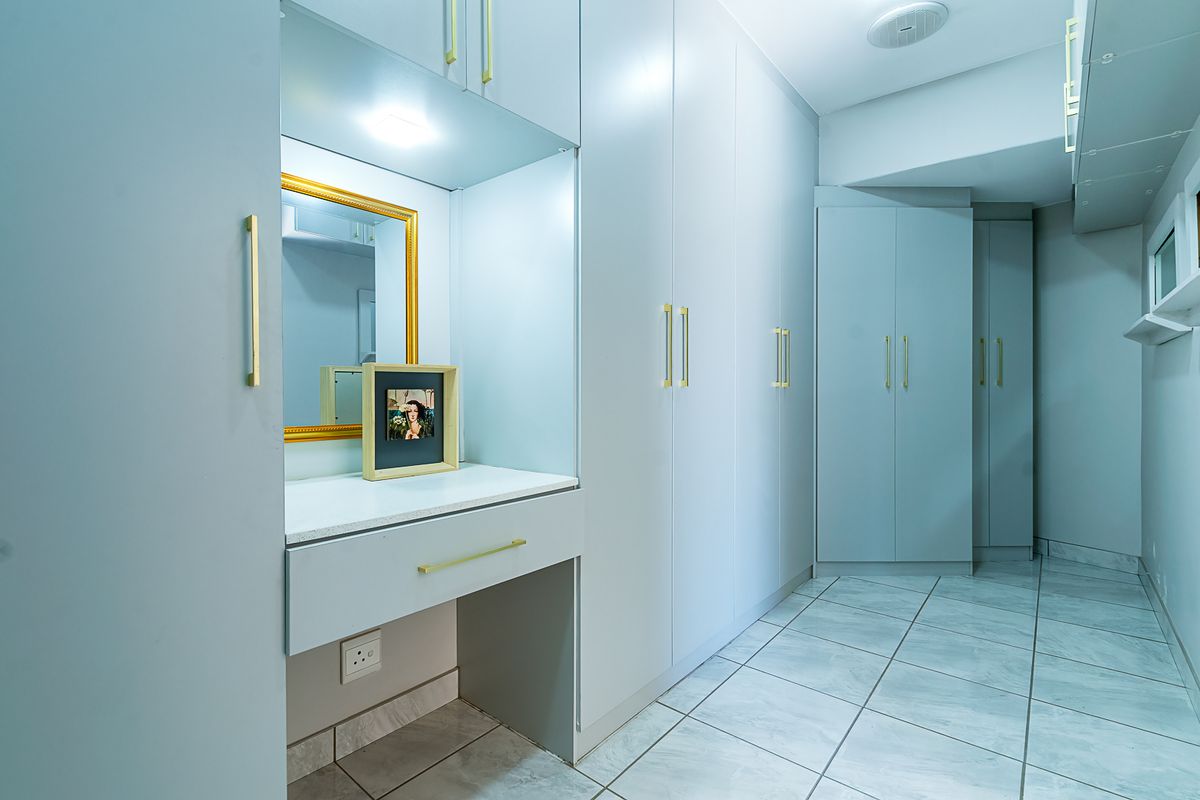 A modern bedroom dressing area featuring extensive built-in cabinetry, a dedicated vanity station with gold hardware, and clean tiled flooring.