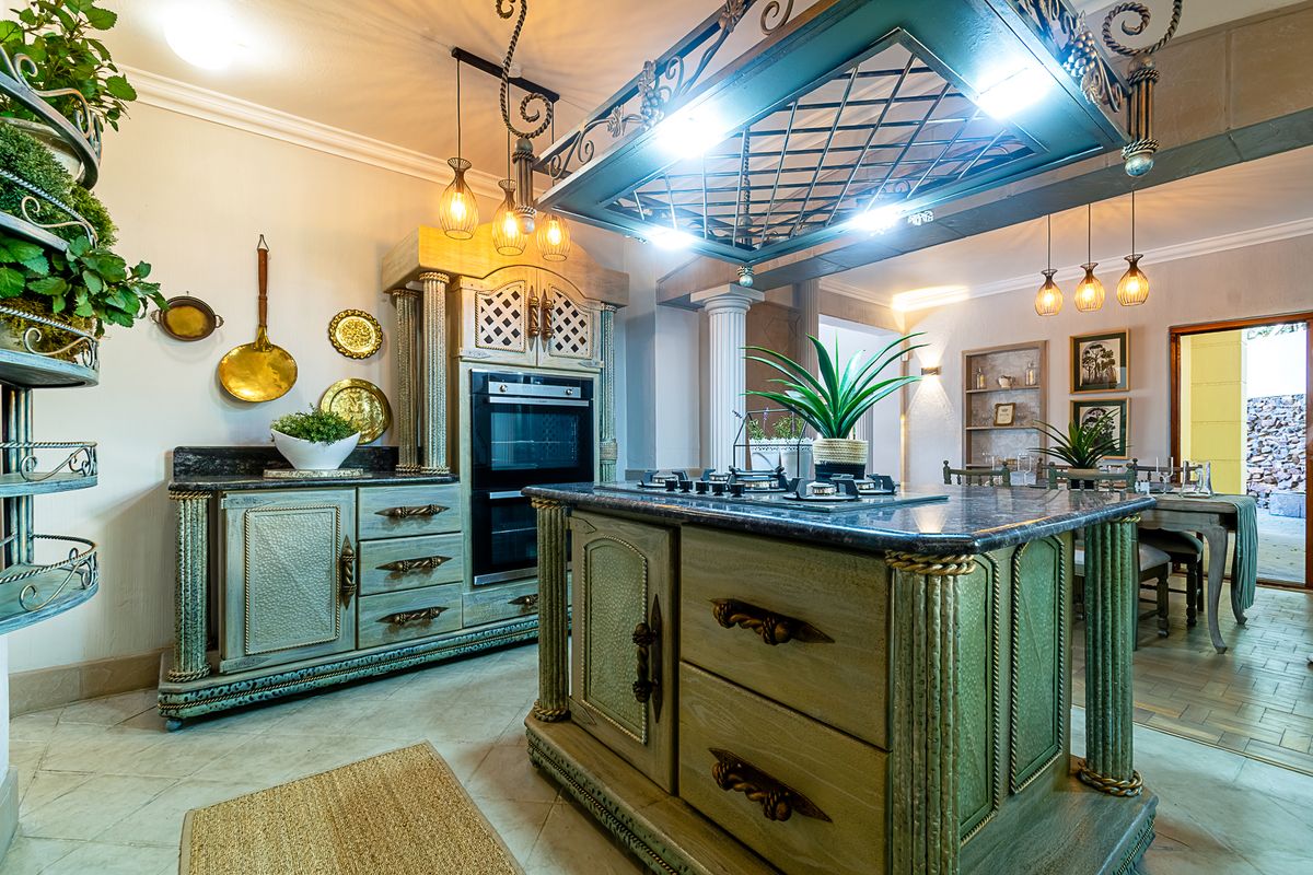 A uniquely styled kitchen featuring custom cabinetry, a central island with a gas cooktop, stone countertops, and an ornate overhead pot rack.
