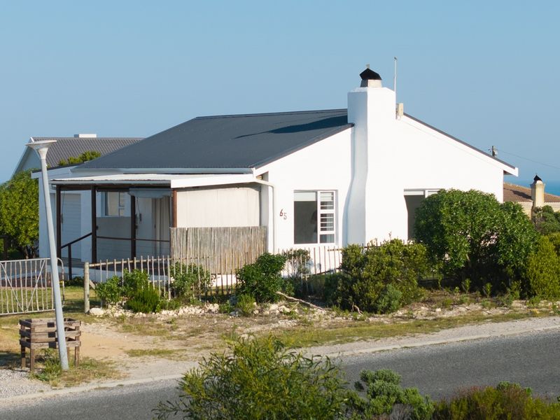 A single-story coastal house featuring a metal roof, prominent chimney, and a covered front patio, situated in a quiet residential street.