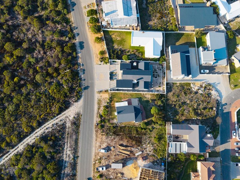 An aerial view of a residential neighborhood showing multiple properties, metal roof structures, and surrounding natural vegetation and road infrastructure.
