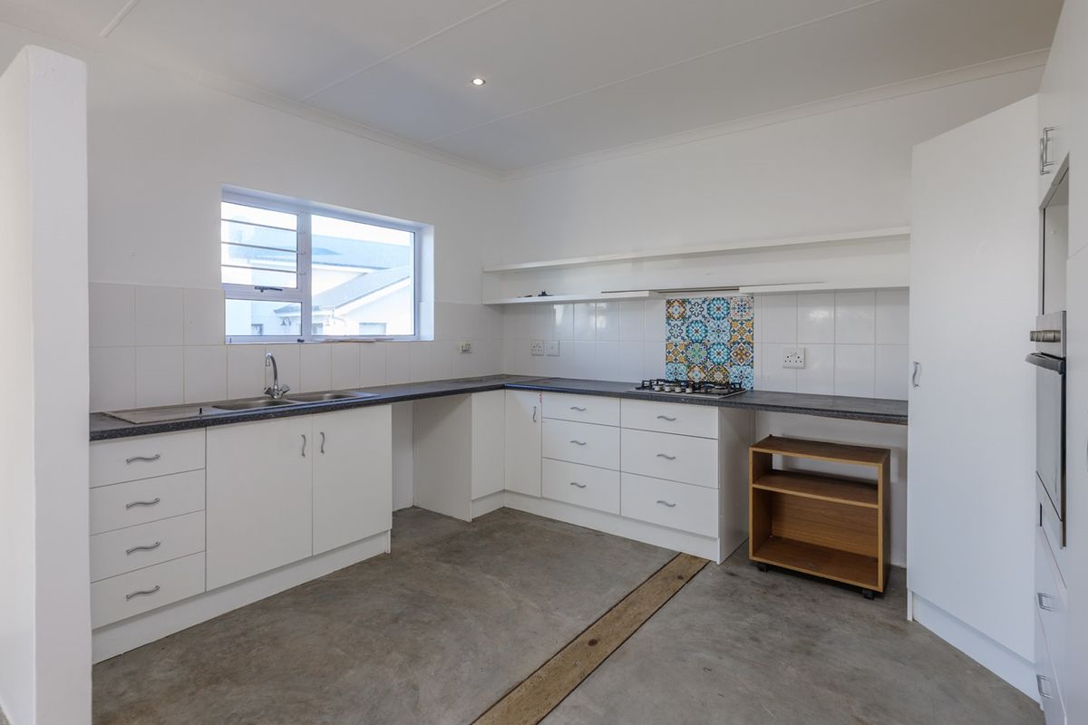A functional, empty kitchen featuring white cabinetry, dark laminate countertops, a gas hob, and a tiled splashback, ready for final flooring finishes.