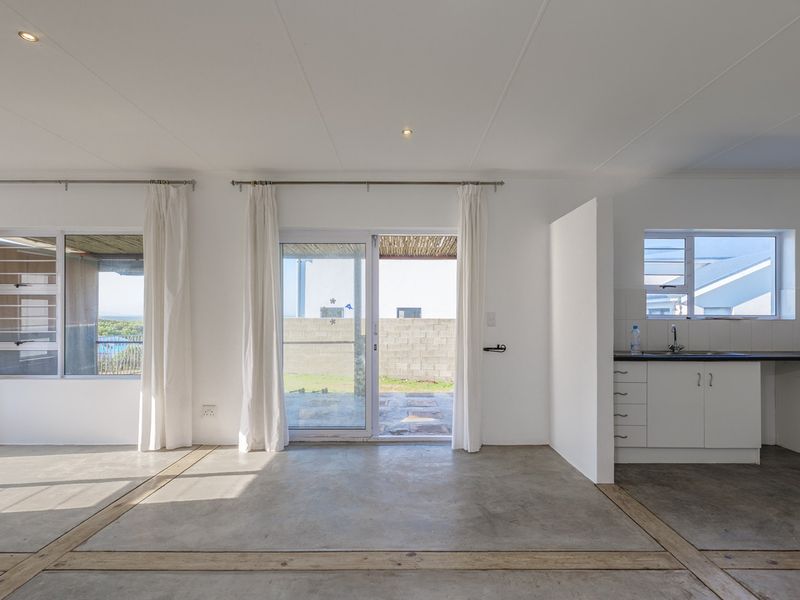 Spacious open-plan living area featuring polished concrete floors, recessed lighting, and a functional kitchen with direct access to the outdoor patio.