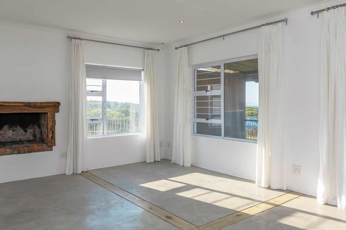 Bright and spacious living area featuring polished concrete floors, a rustic fireplace, and large windows with access to an outdoor patio.