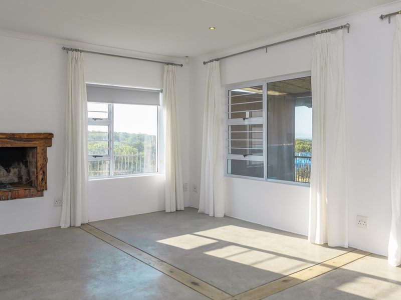 Bright and spacious living area featuring polished concrete floors, a rustic fireplace, and large windows with access to an outdoor patio.