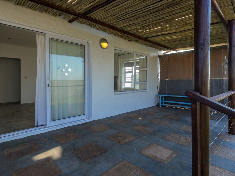 A covered outdoor patio featuring a thatched roof, tiled flooring, and sliding glass doors providing access to the interior living space.