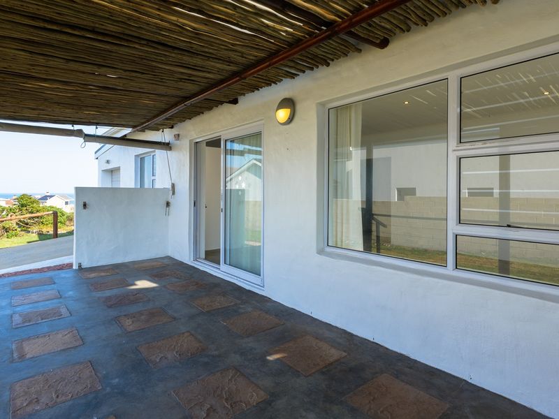 A covered patio area featuring a thatched roof, paved flooring, and sliding glass doors providing access to the interior.
