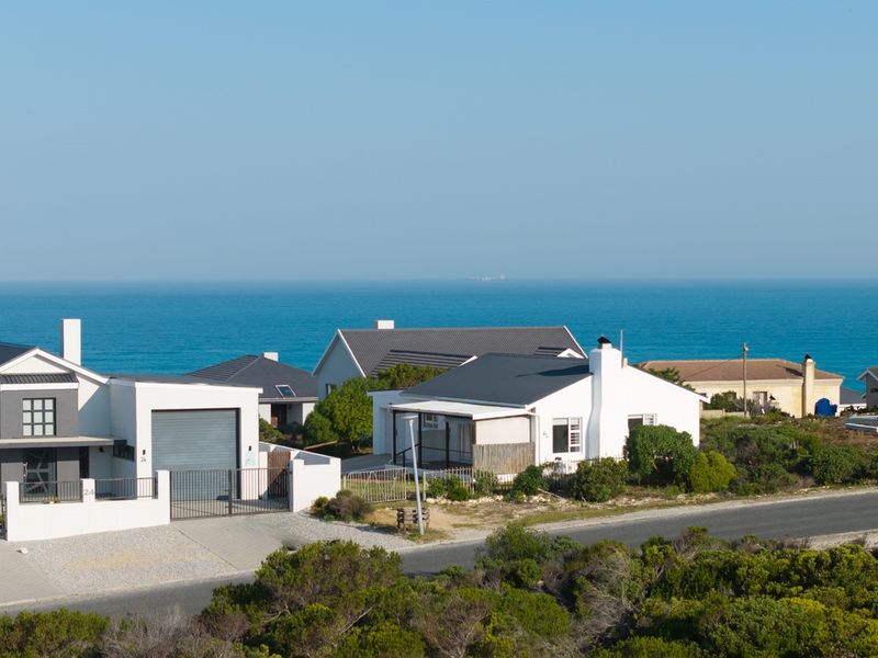 An elevated view of a coastal residential neighborhood featuring modern homes with metal roofs, paved driveways, and scenic ocean views.