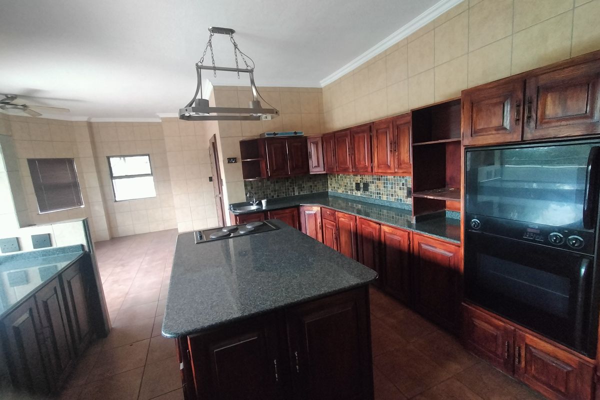 Spacious kitchen featuring dark wood cabinetry, granite countertops, a central island with a built-in hob, and tiled flooring throughout.