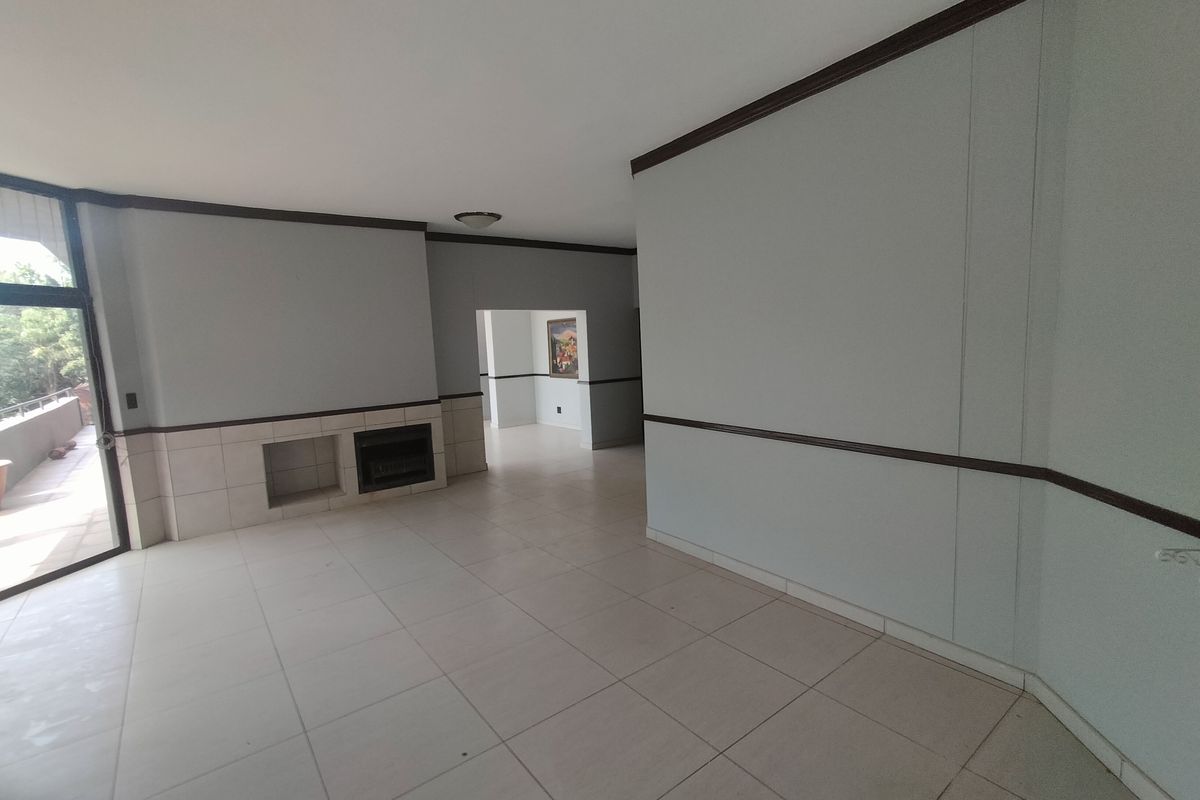 Spacious, empty living room featuring neutral tiled flooring, a built-in fireplace, and access to an outdoor patio area.