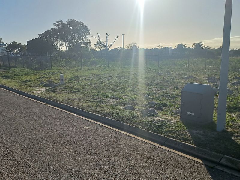 A vacant residential plot featuring a paved curb, perimeter fencing, and existing electrical utility infrastructure.