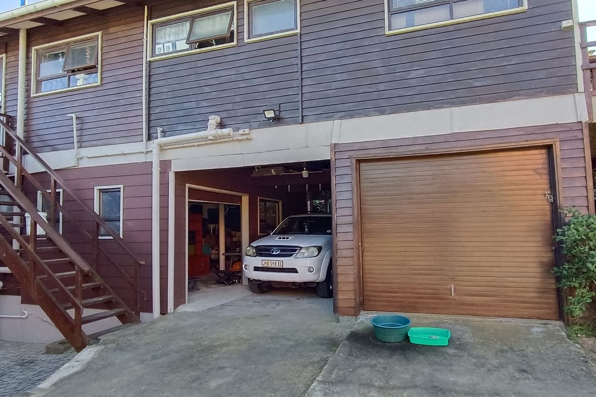 Rear elevation of a timber-clad house featuring an external staircase, a garage with a roll-up door, and a concrete driveway area.
