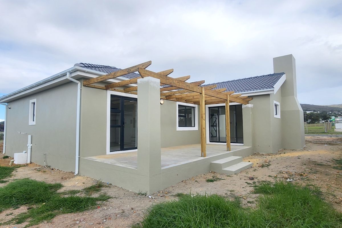 Rear view of a modern house featuring a timber pergola over a concrete patio, sliding glass doors, and an external chimney.