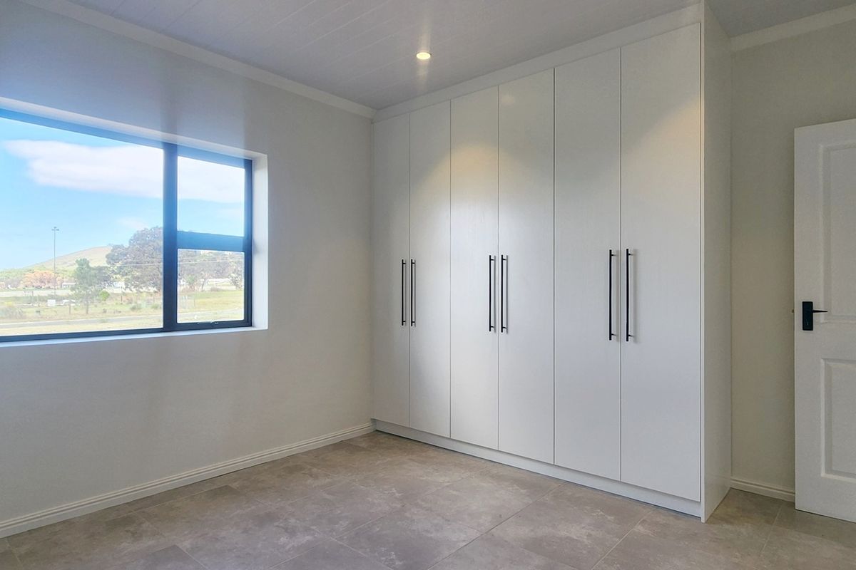 A bright, modern bedroom featuring neutral tiled flooring, ample built-in cupboard storage, and a large window providing natural light and scenic views.
