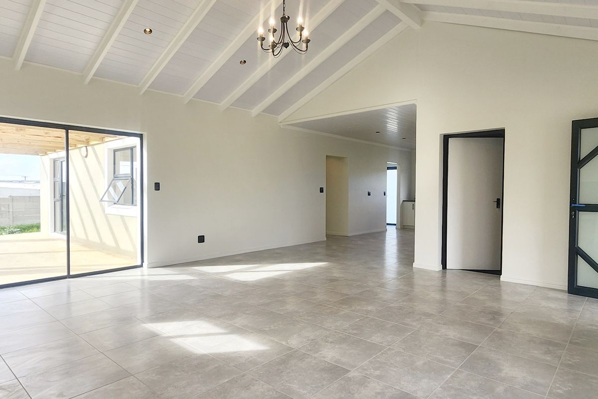Spacious open-plan living area featuring vaulted ceilings with exposed rafters, large format floor tiles, and sliding doors leading to an outdoor patio.