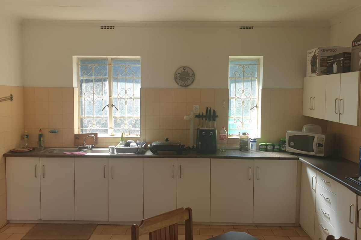 A functional kitchen featuring white built-in cabinetry, laminate countertops, a stainless steel sink, and tiled backsplash with security bars on the windows.