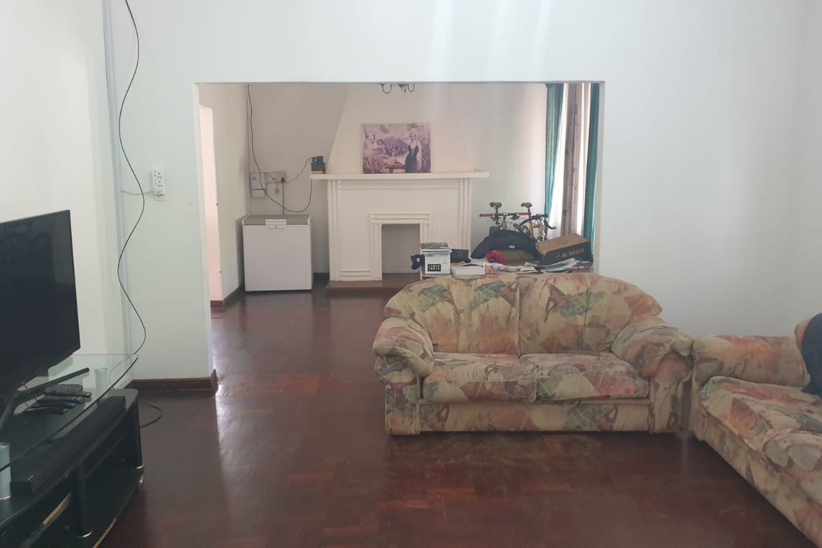 A living room featuring parquet flooring and a central fireplace, offering a spacious layout with potential for modernization.