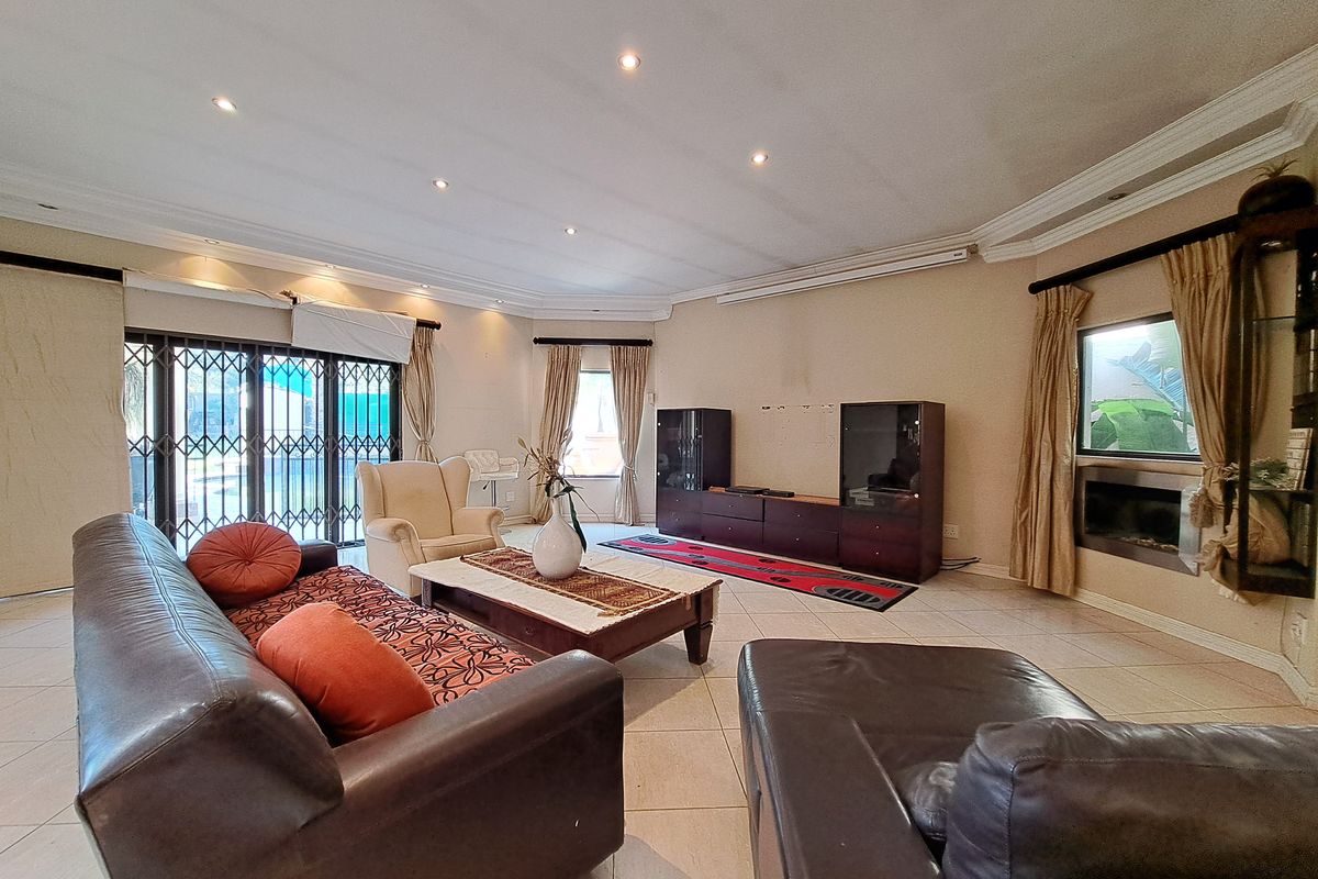 Spacious living room featuring tiled flooring, recessed downlights, decorative cornicing, and a built-in fireplace with access to the outdoor area via security gates.