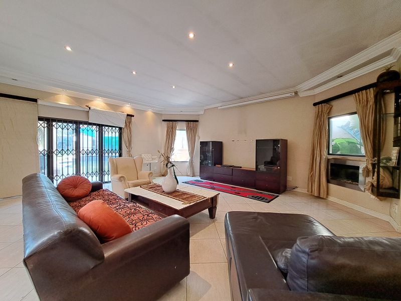 Spacious living room featuring tiled flooring, recessed downlights, decorative cornicing, and a built-in fireplace with access to the outdoor area via security gates.