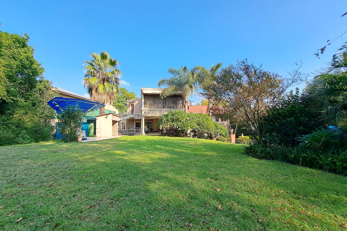 A spacious rear garden featuring a well-maintained lawn, mature trees, and a multi-level house with a balcony and patio area.