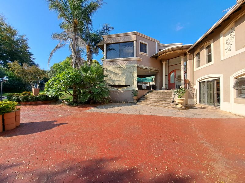 Spacious rear exterior featuring a large brick-paved patio, covered terrace area, and stone staircase leading to the main entrance.