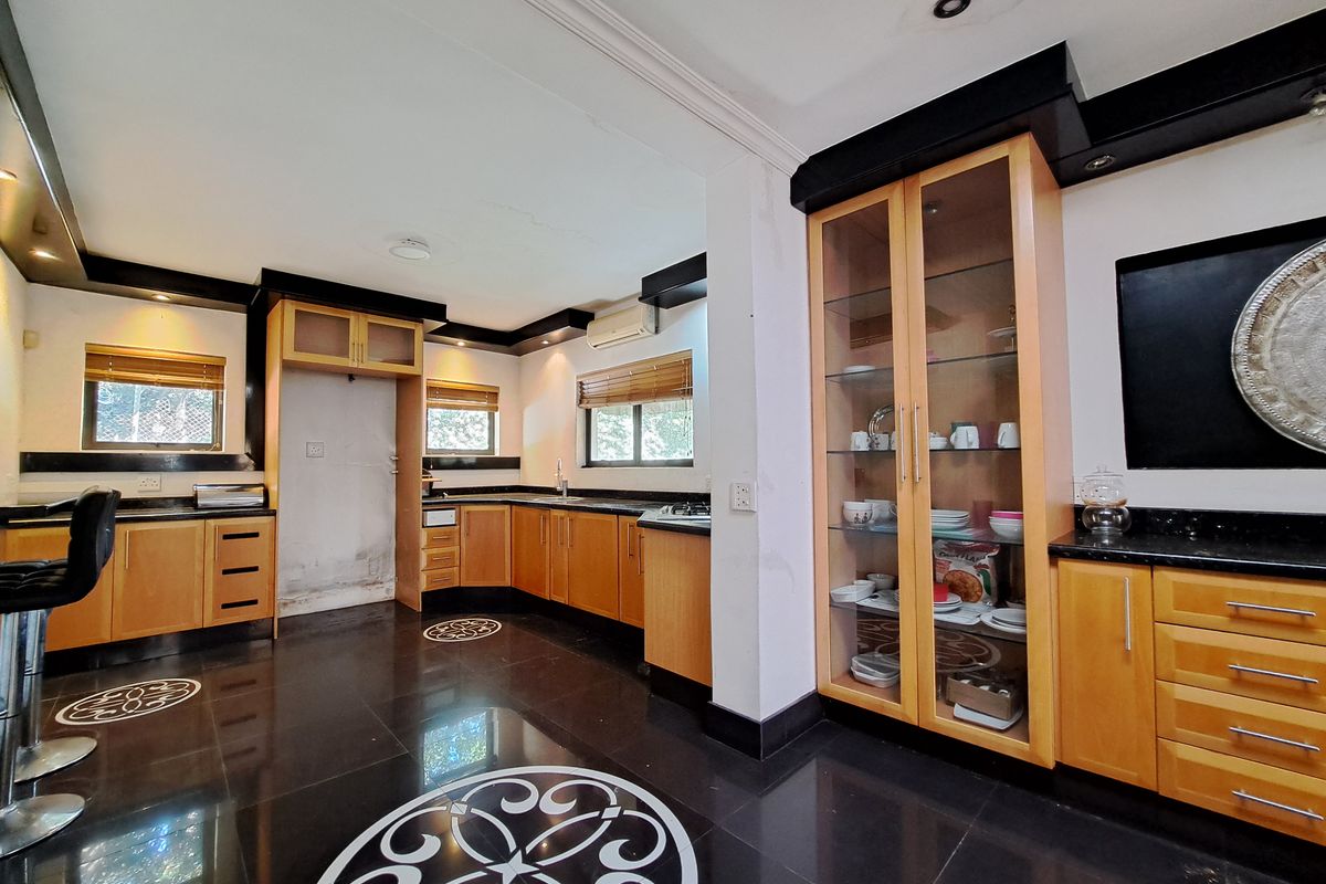 Spacious kitchen featuring wooden cabinetry, granite countertops, integrated hob, and a glass-fronted display cabinet with dark tiled flooring.
