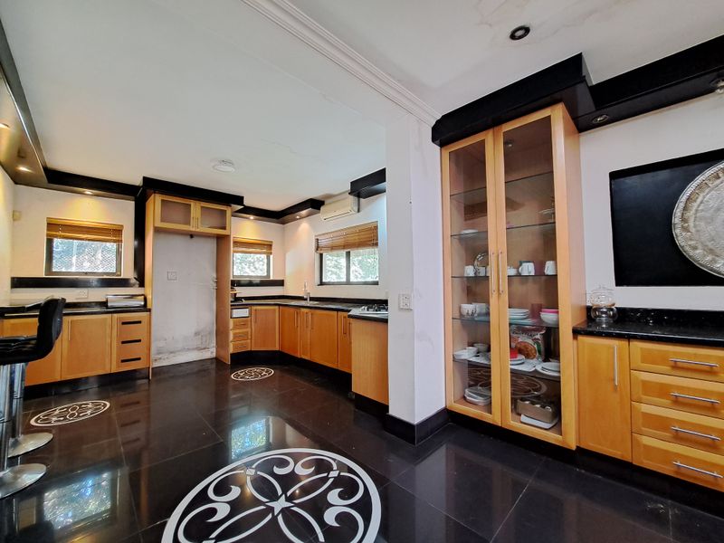 Spacious kitchen featuring wooden cabinetry, granite countertops, integrated hob, and a glass-fronted display cabinet with dark tiled flooring.