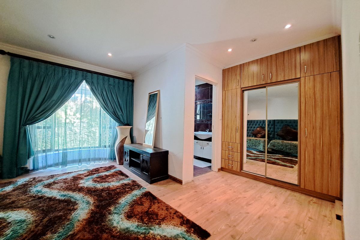 Spacious bedroom featuring extensive built-in wooden cupboards with mirrored doors, laminate flooring, recessed lighting, and direct access to an en-suite bathroom.