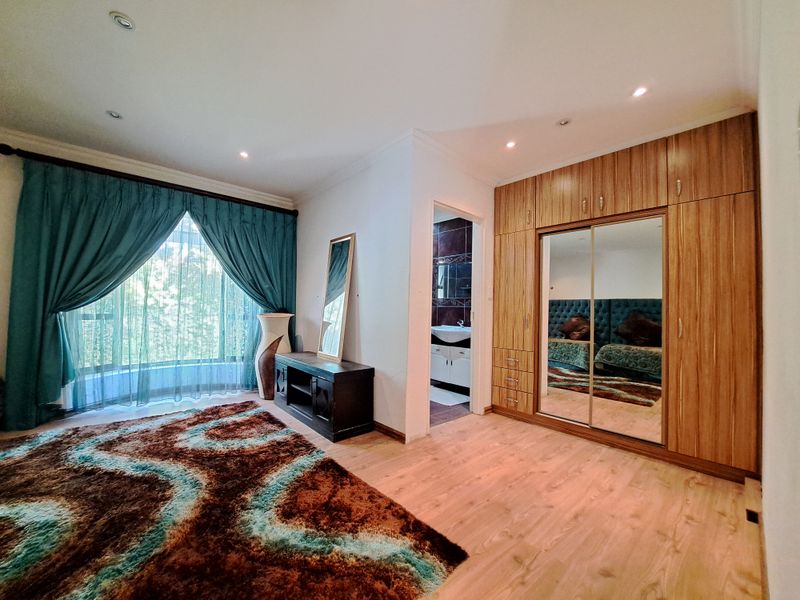 Spacious bedroom featuring extensive built-in wooden cupboards with mirrored doors, laminate flooring, recessed lighting, and direct access to an en-suite bathroom.