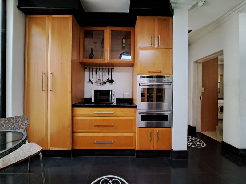 A well-maintained kitchen featuring warm wood cabinetry, a double wall oven, and contrasting black granite countertops with dark floor tiles.