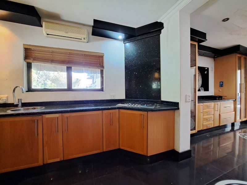 A functional kitchen featuring wooden cabinetry, granite countertops, a gas hob, and a stainless steel sink, with integrated air conditioning and recessed lighting.