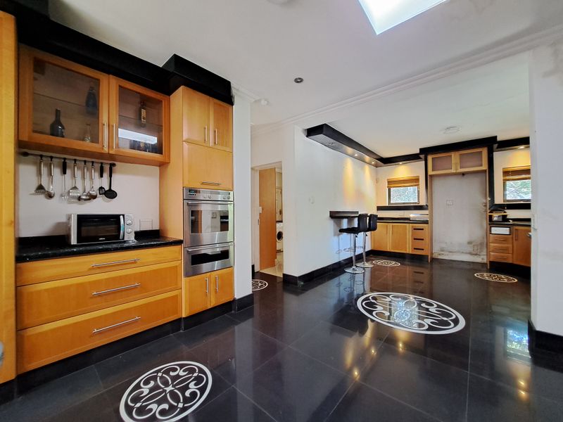Spacious kitchen featuring wooden cabinetry, black granite countertops, built-in oven, and a skylight, with tiled flooring throughout.