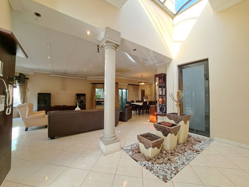 Spacious open-plan living and dining area featuring a central structural column, tiled flooring, recessed lighting, and a unique indoor water feature under a skylight.
