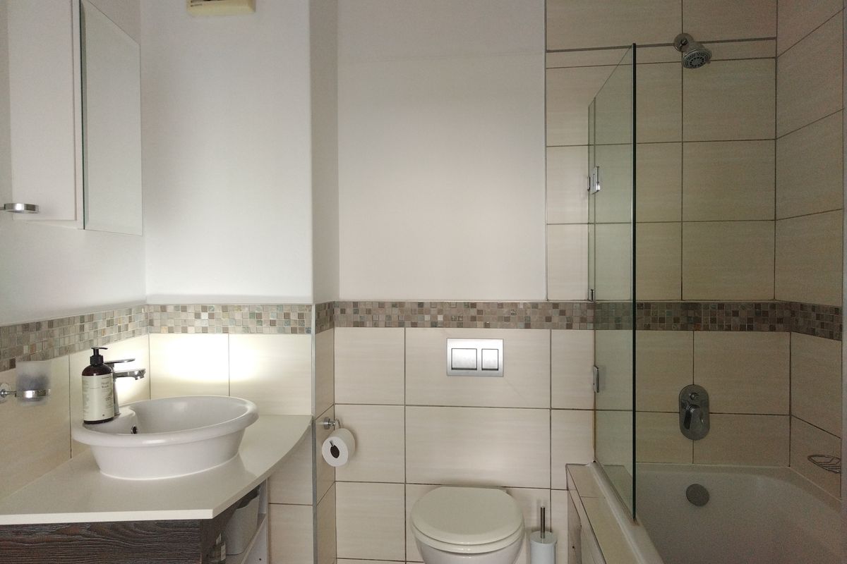 Modern bathroom featuring a vessel sink, wall-hung toilet with dual-flush plate, and a bathtub with a glass shower screen and tiled finishes.