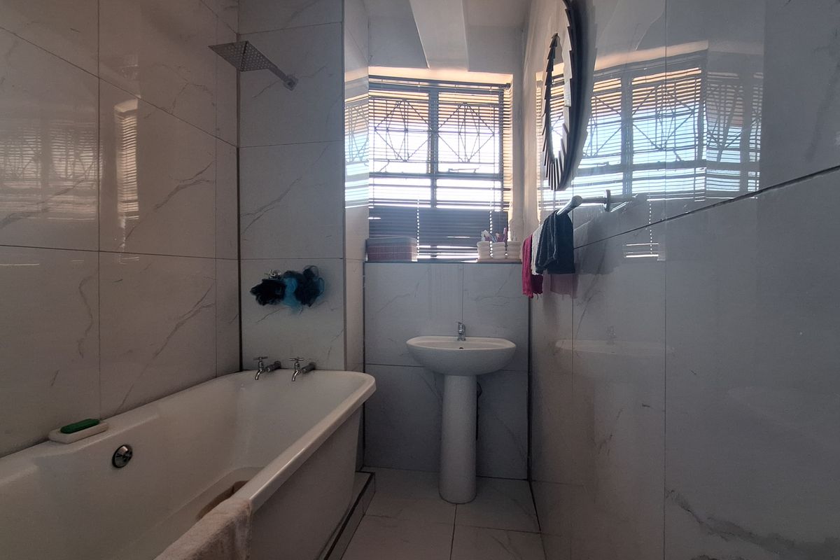 A modern bathroom featuring floor-to-ceiling marble-look tiles, a pedestal basin, and a bathtub with an overhead shower fixture.