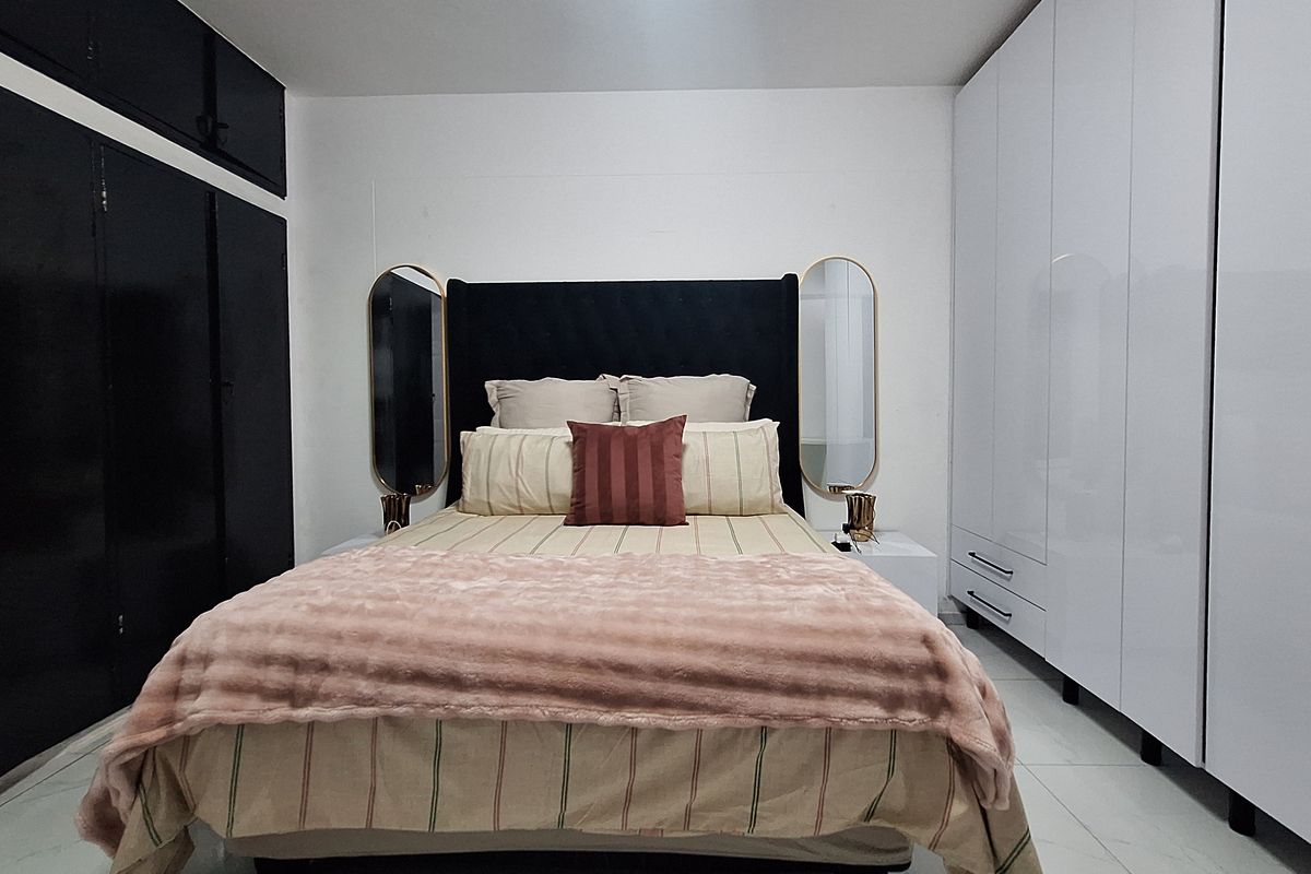 A well-maintained bedroom featuring extensive built-in white cabinetry, dark accent storage, and polished tiled flooring.