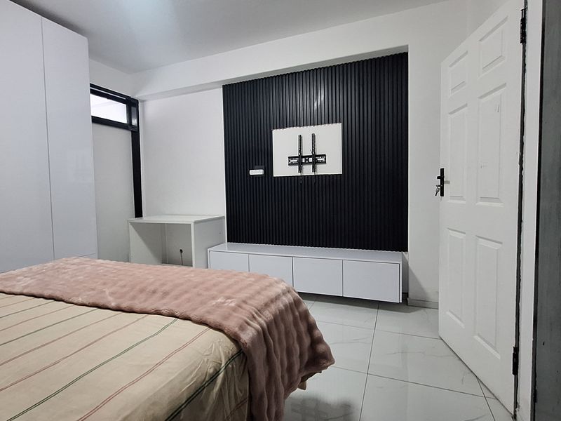 Modern bedroom featuring a sleek slatted feature wall, built-in media console, and floor-to-ceiling white wardrobes with polished tile flooring.