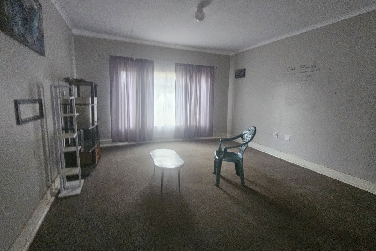 A sparsely furnished living room featuring carpet flooring and neutral wall tones, offering a blank canvas for potential interior design updates.