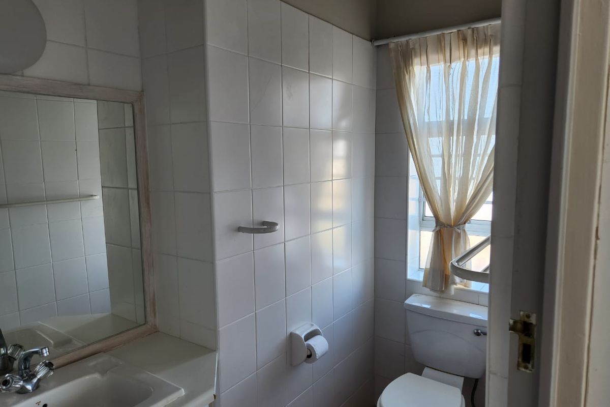 A functional bathroom featuring tiled walls, a vanity basin with a mirror, and a standard toilet, offering a clean but dated aesthetic.