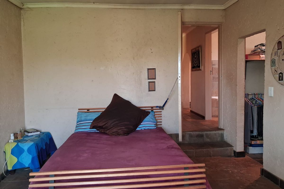 A bedroom featuring tiled flooring, a walk-in closet, and direct access to an en-suite bathroom, requiring cosmetic updates to the wall finishes.