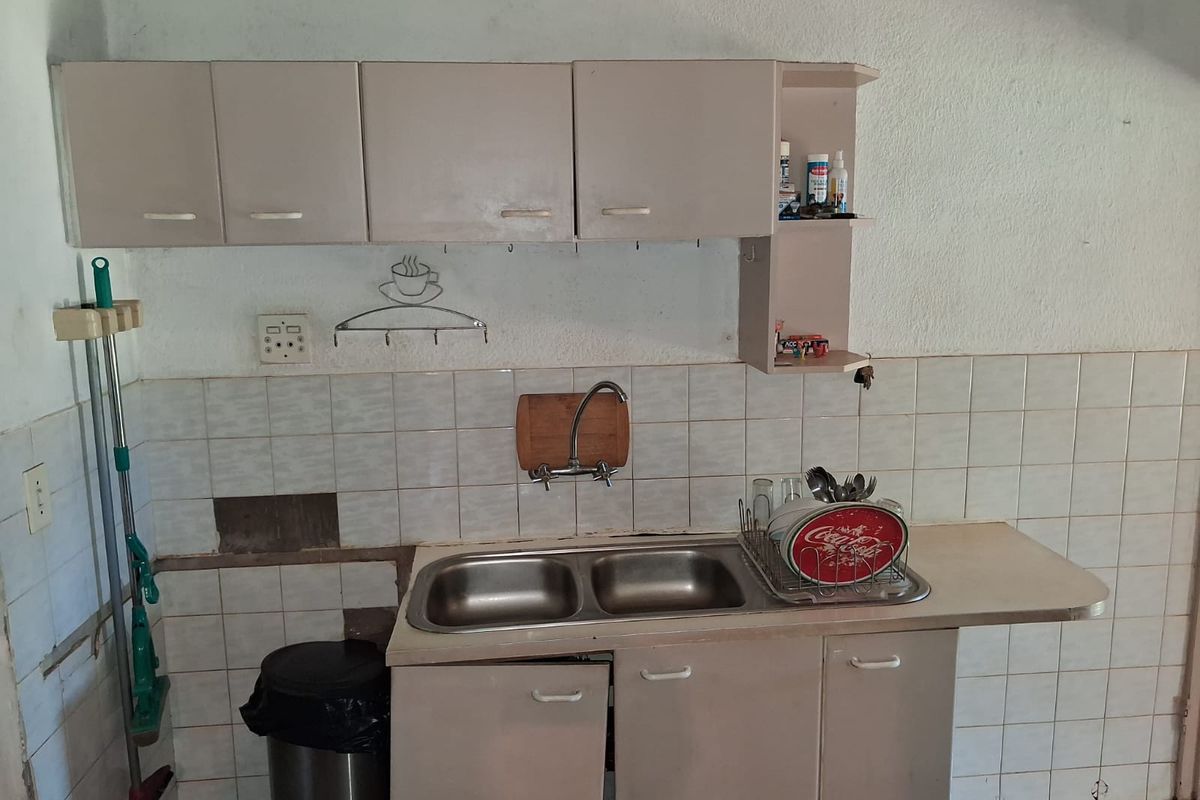 A compact kitchen area featuring a double bowl stainless steel sink, wall-mounted and base cabinetry, and a tiled backsplash with some visible wear.