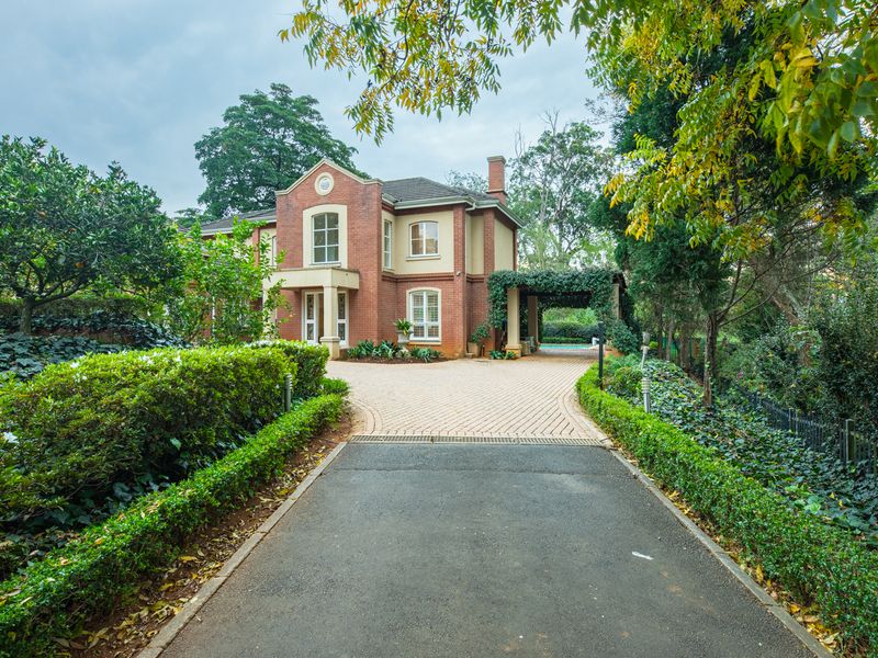 A well-maintained double-story brick residence featuring a paved driveway, lush landscaped gardens, and a covered outdoor patio area.